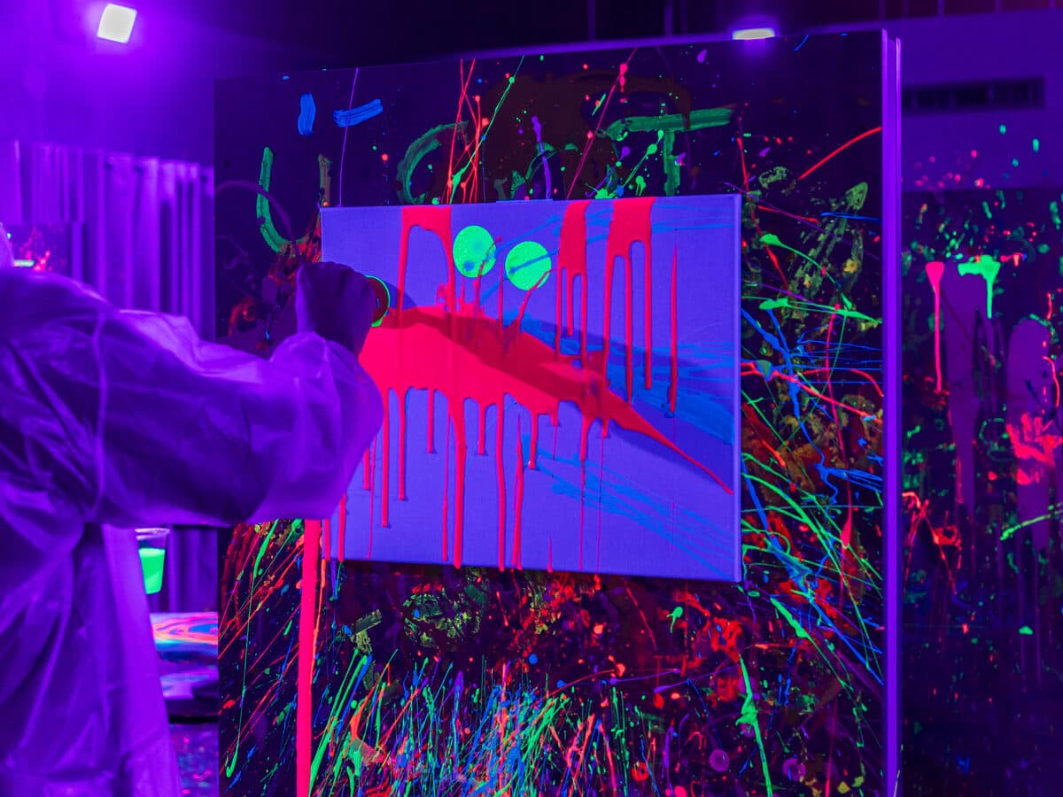 Neon paint dripping down a canvas under blacklight